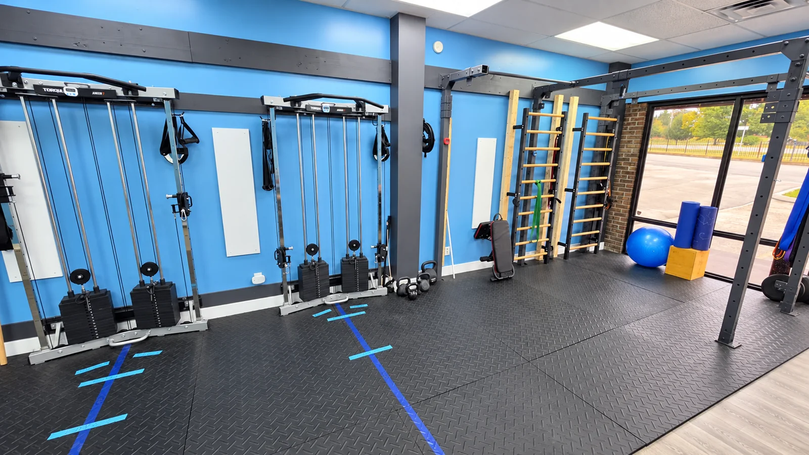 Optimal Fitness gym with blue walls, Torque ANKER 7 cable machines and wooden Swedish stall bars